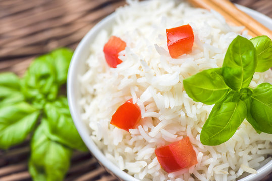Cooked basmati rice in a bowl with chipsticks, tomato and basil