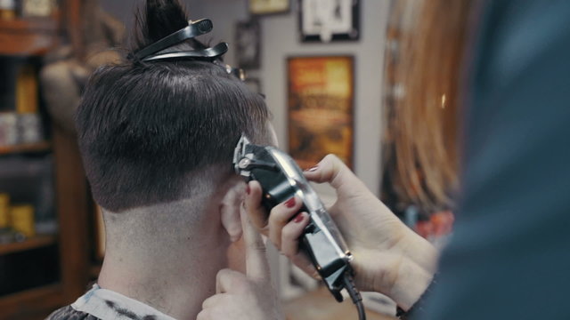 Woman barber cuts the hair of the client with clipper at barbershop, slow motion