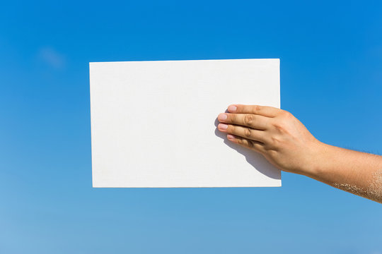 Blank white board in hand against blue sky background