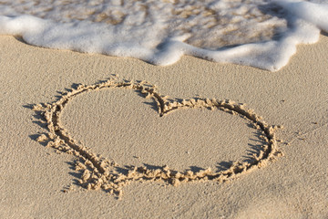Shape of heart on sandy beach with wave's foam