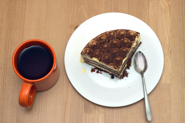Breakfast. A piece of sponge cake on a white plate with a teaspoon and orange cup of tea on the wooden table surface. Top view closeup