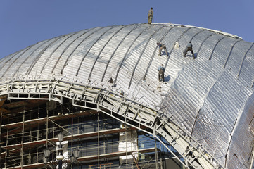 Construction workers-roofers, tied with ropes for protection work on the roof of a new building -...