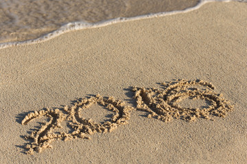 Inscription 2016 on sandy beach with wave's foam