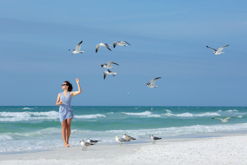 Fototapeta na wymiar Young woman feeding seagulls on tropical beach, Florida