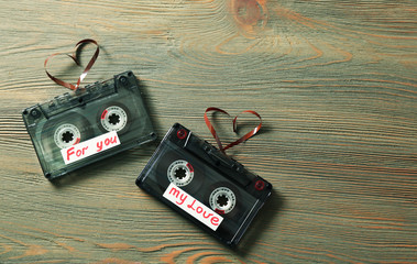 Retro audio cassettes with tapes in shape of hearts on wooden background