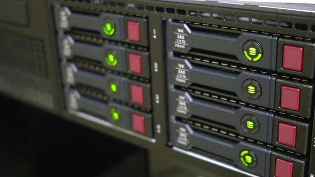Close up of green LED lights on multiple hard drives of a large server blink on and off in a rotating alternating pattern.