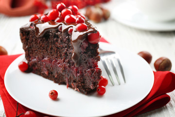Piece of chocolate cake with cranberries on plate with nuts on wooden table, closeup