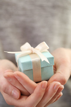 Female hands holding beautiful small gift wrapped with satin ribbon.