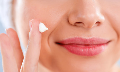 Beautiful young woman applying a creme on her face isolated on gray background