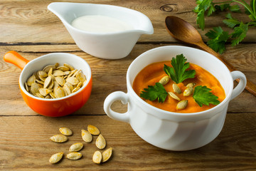 Roasted pumpkin squash cream soup with parsley and pumpkin seeds in the white bowl on the dark wooden background with checkered linen napkin