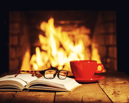 Red cup of coffee or tea, glasses and old book on wooden table n