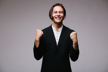 Business world. View of excited young businessman keeping arms raised and expressing positivity while standing against white background