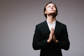 Side view of concentrated young man in white shirt holding hands clasped near face and looking away while standing against grey background