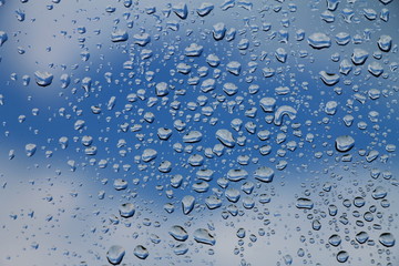 Rain drops on window with blue cloudy sky in background