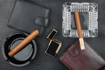 Golden lighter with cigar and purse lying on a black skin