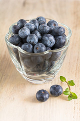 Frische Heidelbeeren in einer Glasschale stehen auf einem Holzbrett