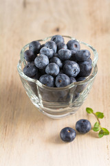 Frische Heidelbeeren in einer Glasschale stehen auf einem Holzbrett