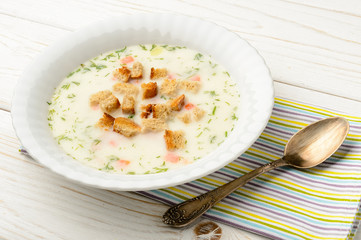 Cheese soup in white bowl on white wooden table.