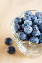 Frische Heidelbeeren in einer Glasschale stehen auf einem Holzbrett