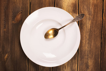 Top view of white empty plate with vintage spoon over grunge wooden background. Toned image