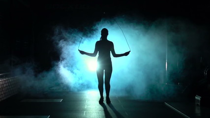 Sporty woman jumps on the jumping rope in silhouette and smoke, front view, slow motion - Powered by Adobe