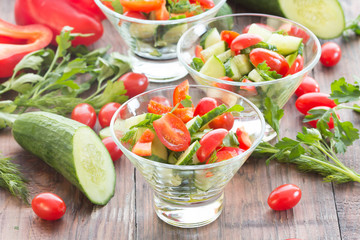 Vegetables salad in glass bowls and ingredients - tomatoes, cucumber, paprika, cilantro on wooden dark background