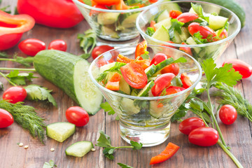 Three glass bowls with a salad of fresh vegetables and ingredients - tomato, cucumber, bell pepper on a dark wooden background
