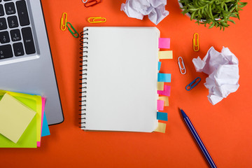 Office table desk with set of colorful supplies, white blank note pad, cup, pen, pc, crumpled paper, flower on red background. Top view and copy space for text