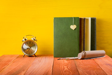 Stack of hardback books, diary on wooden deck table and yellow background. Back to school. Copy Space. Education background