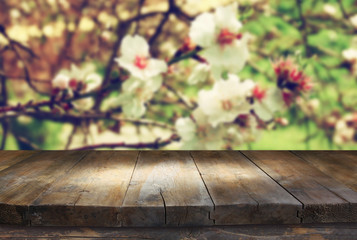 Fototapeta premium wooden rustic table in front of spring white cherry blossoms tree. vintage filtered image. product display and picnic concept 