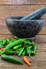 Red and green chilli peppers on rustic wood background with granite mortar and pestle