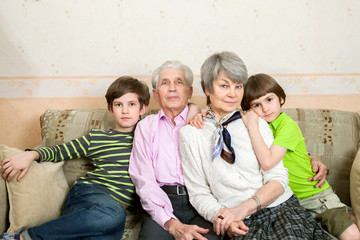 Grandfather, grandmother and grandchildren sit on sofa at the home