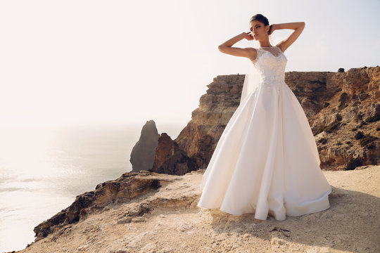fashion outdoor photo of gorgeous beautiful bride with dark hair wears elegant wedding dress posing at seacoast  