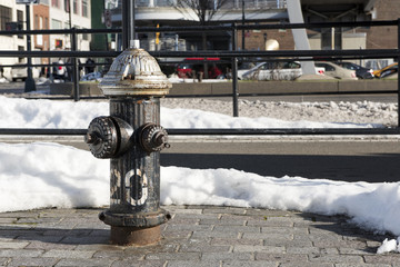 Black, New York roadside fire hydrant with a silver top, showing signs of age/rust. Landscape orientation  