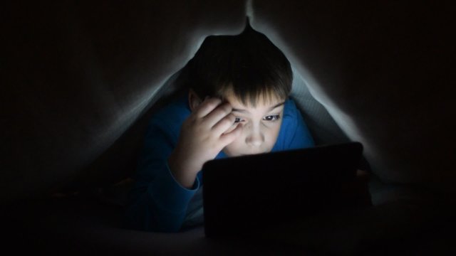 Young boy watches tablet in bed