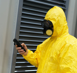 Worker in protective chemical suit checking radiation with geiger counter.