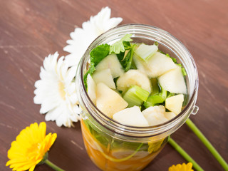 Mixer glass with fruit and vegetables for a smoothie (banana, orange juice, pear, ginger and celery) with spring color flowers around on brown wooden table
