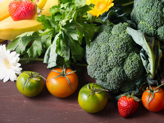 Spring fruit and greens assortment (broccoli, celery, tomatoes, bananas and strawberries) on bwon wooden table