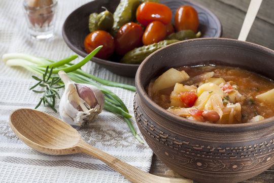 Traditional ukrainian vegetable soup - borsch, marinated tomatoes and cucumbers, sour cream, sliced bread, herbs and garlic at dark wooden table.