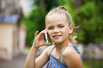 Little girl talking on cell phone against green of Park in summe