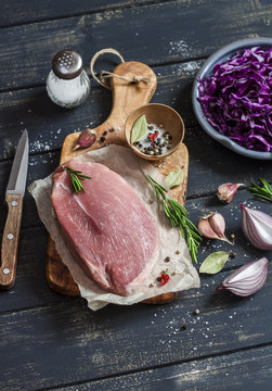 Meat, red cabbage, onion, garlic, spices and herbs- raw ingredients for cooking delicious and healthy lunch. On dark  wooden  background