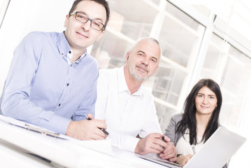 Obraz premium Successful business people interacting, discussing and sharing ideas in bright modern office. Teamwork concept. Focus on man in the middle. People looking at camera