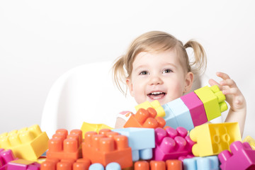 Fototapeta na wymiar Adorable little girl sitting on chair smiling and playing with colorful toy blocks