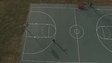 Young boy attempting shot at basketball rim, seen from aerial view.