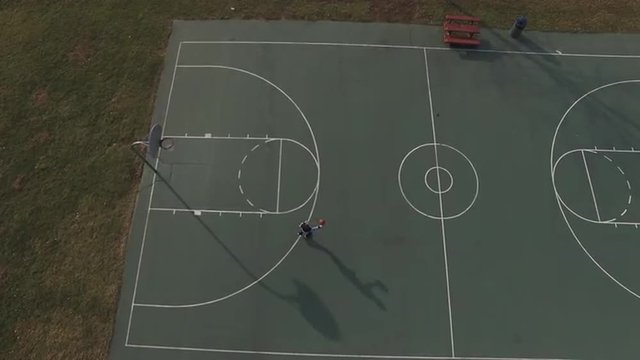 Young boy attempting shot at basketball rim, seen from aerial view.