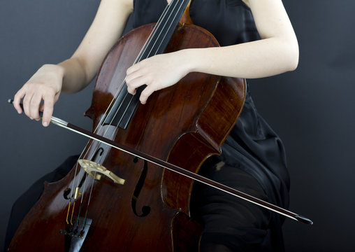 A young girl plays the cello in the dark. Hands on cello
