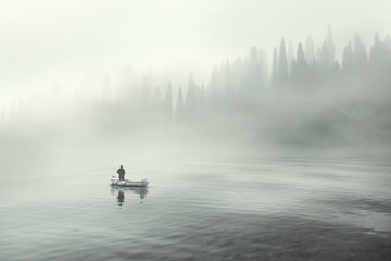 Naklejka premium Man fishing on a boat in a mistic foggy lake