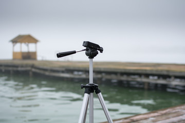 Camera tripod. Photo was taken outdoor in a park, near lake. It was very early in the morning, with fog all around photo stand.
