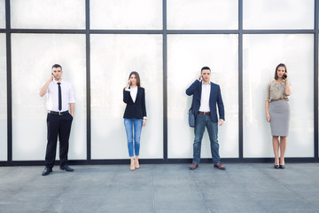 Fototapeta premium Four young business people talking on mobile phones in front of contemporary office building