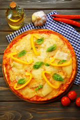 Tasty pizza decorated with basil and pepper on wooden background